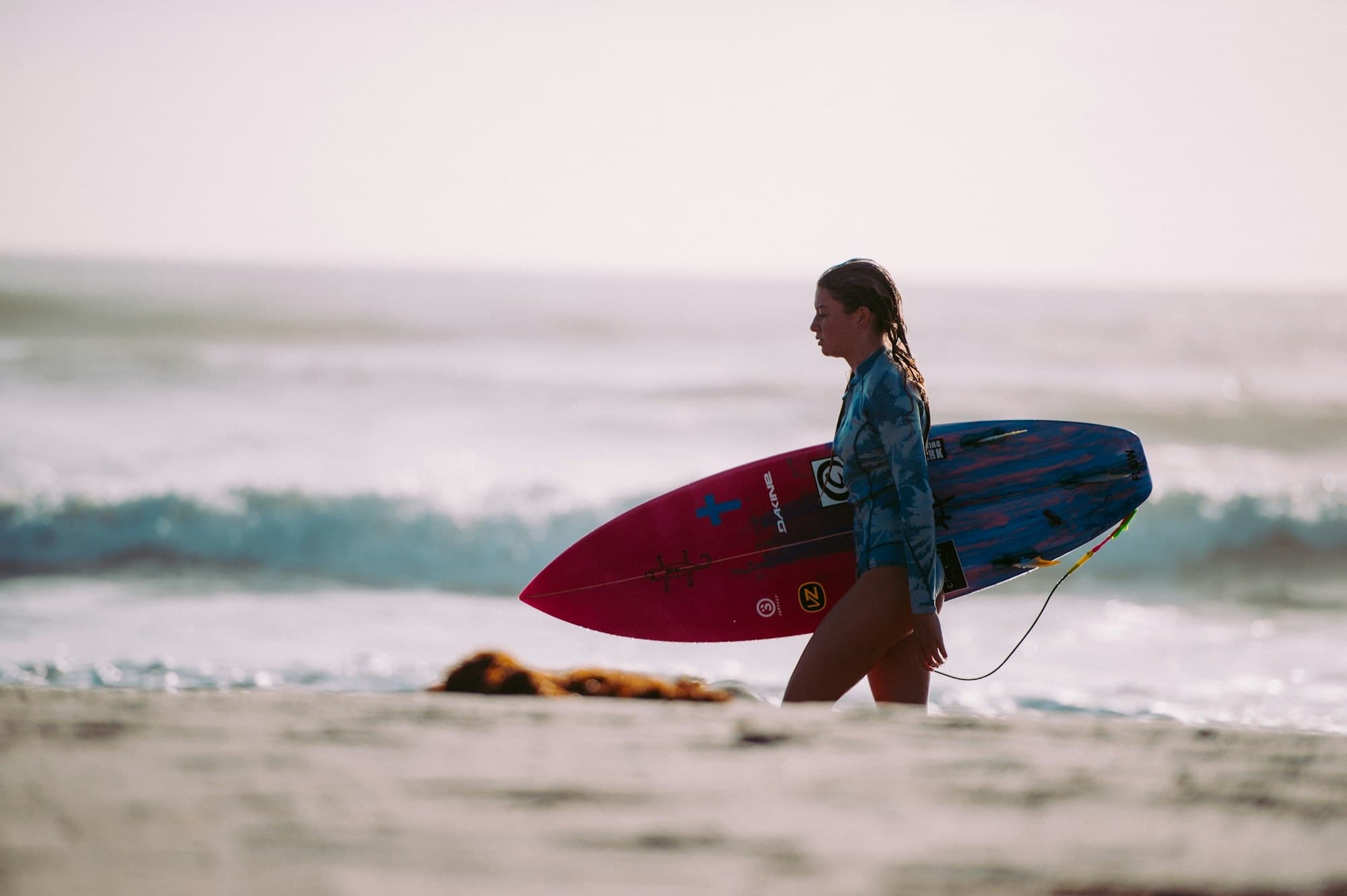 Woman carrying a surfboard along the beach